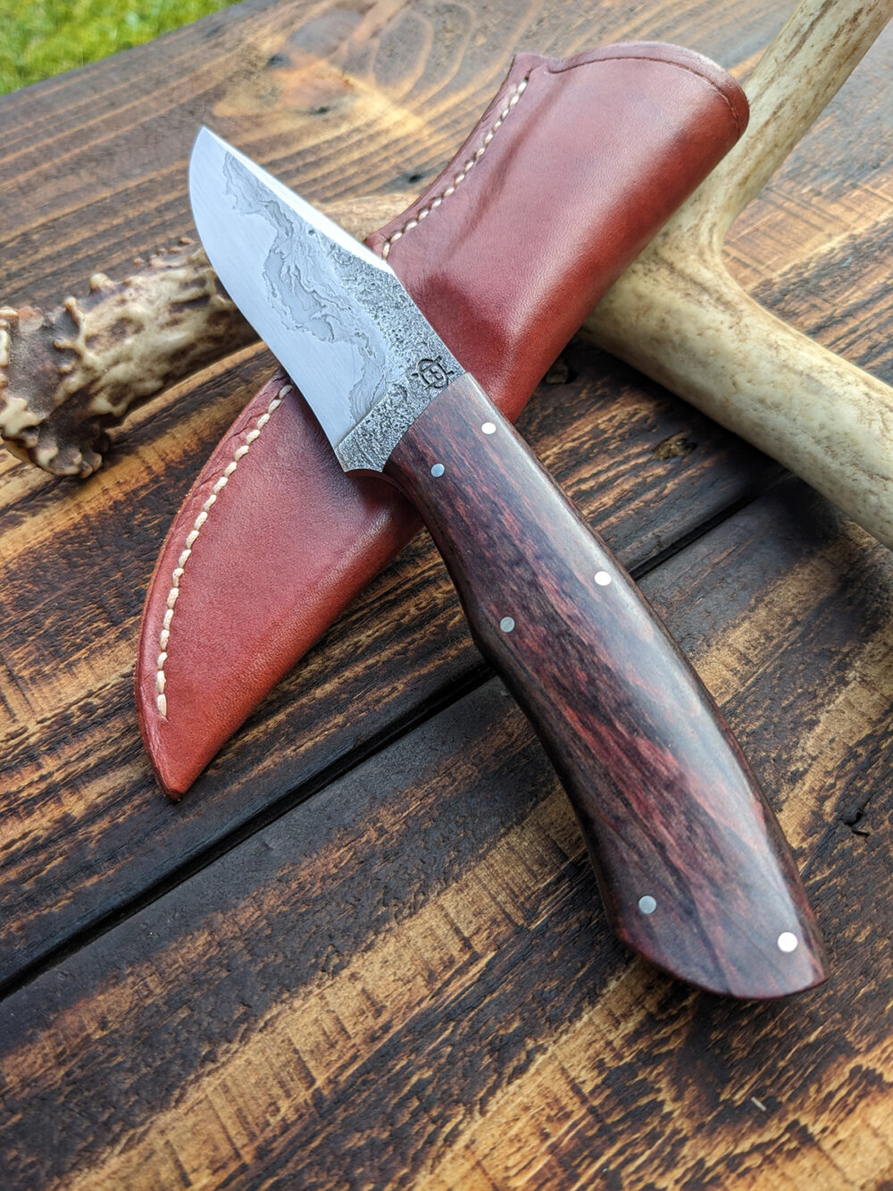 A recurve hunting knife with chainsaw chain damascus cladding.