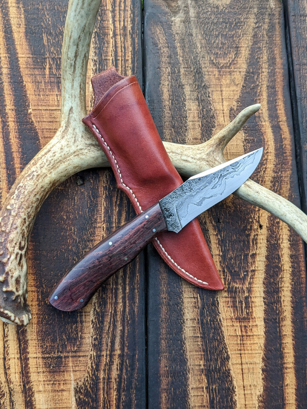 A recurve hunting knife with chainsaw chain damascus cladding.