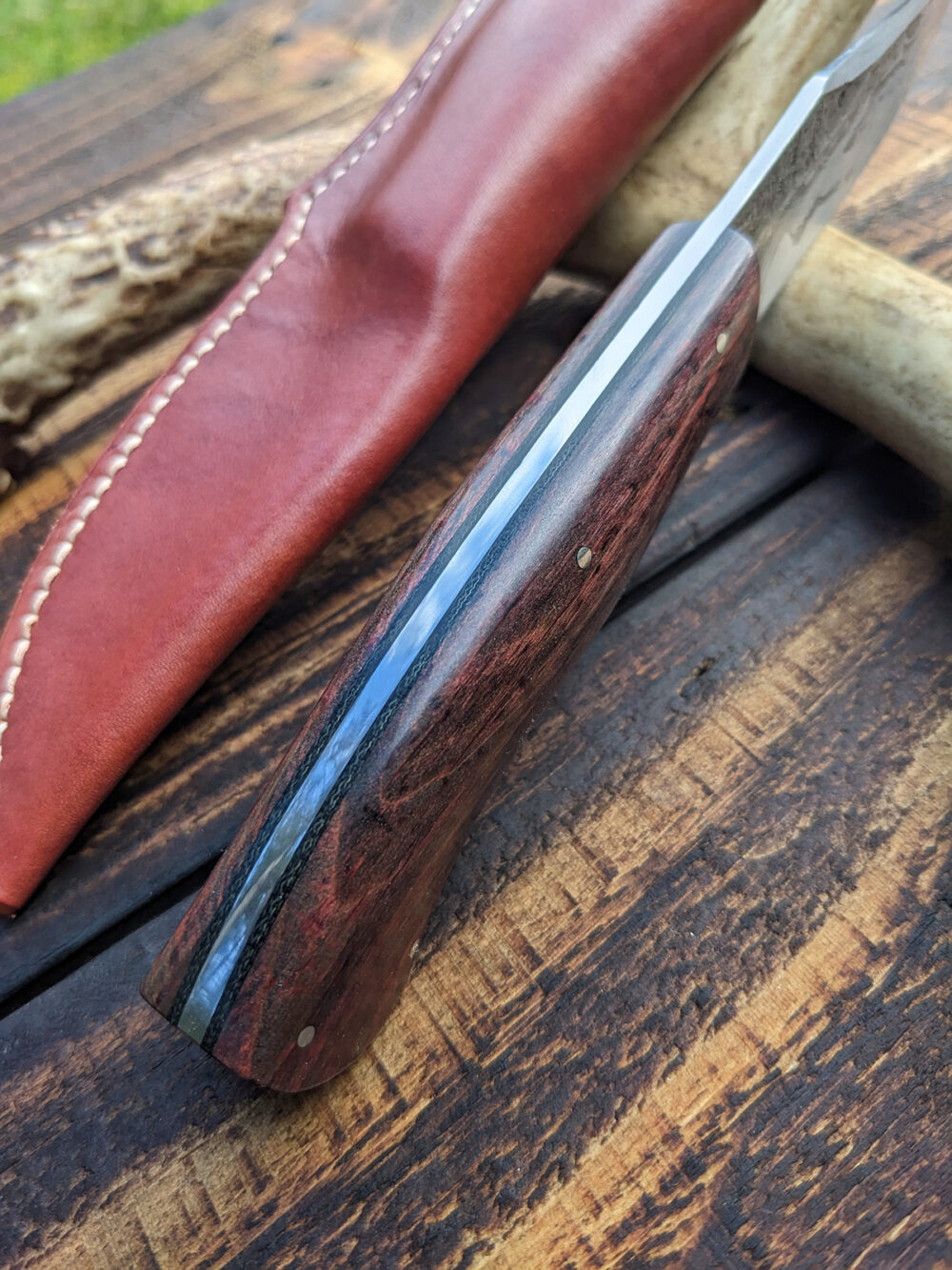 A recurve hunting knife with chainsaw chain damascus cladding.