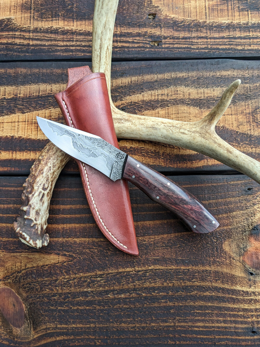 A recurve hunting knife with chainsaw chain damascus cladding.