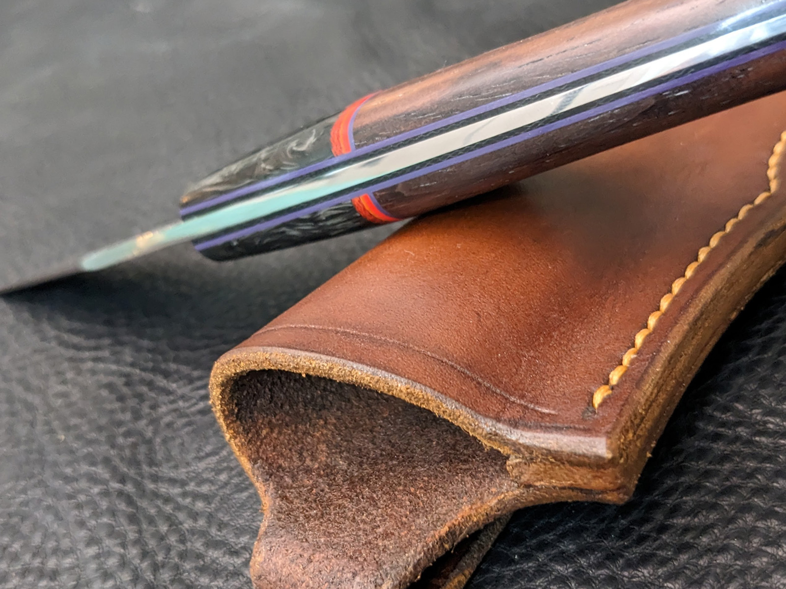 The spine of a recurve hunting knife with purple and black liners.