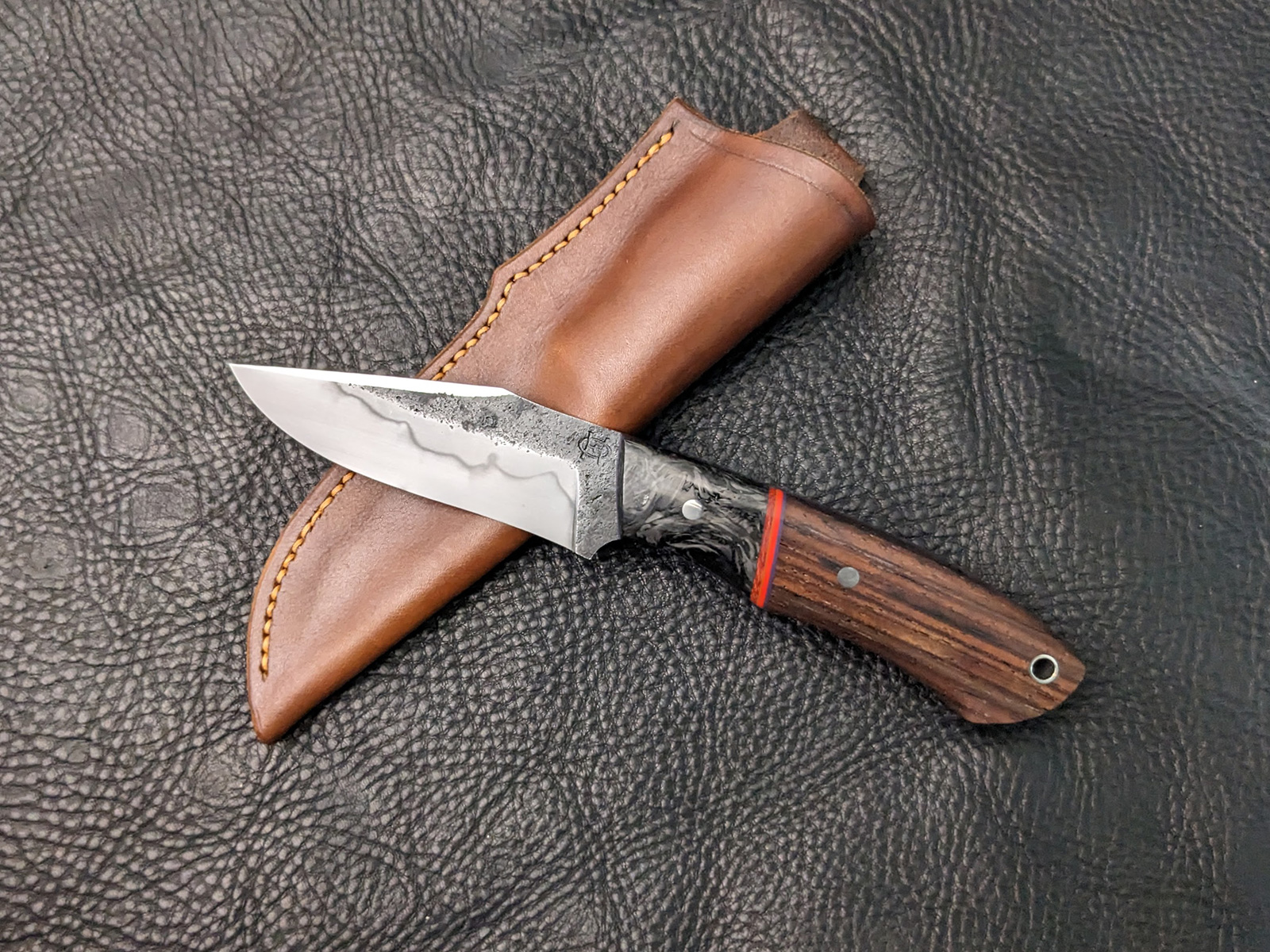 A recurve hunting knife with carbon fiber bolsters and cocobolo handle.